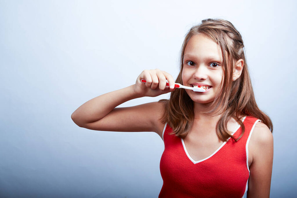 a cheerful beautiful girl of 11 years old brushes her teeth on a white background - Photo, Image