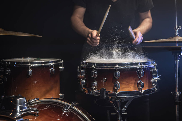 Een mannelijke drummer speelt snare drum met drumsticks in een donkere kamer. - Foto, afbeelding