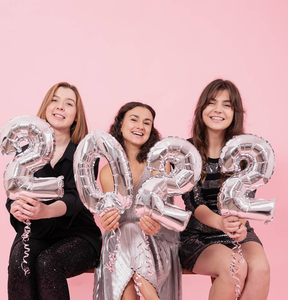 Una compañía de novias alegres sobre un fondo rosa con globos de lámina de plata en forma de números 2022, celebrando el nuevo año. - Foto, imagen