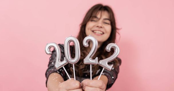 Chica alegre sobre un fondo rosa sonríe y sostiene los números 2022 en sus manos, celebrando el nuevo año. - Foto, imagen