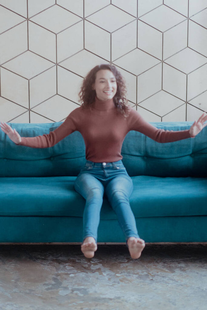 jovem bela mulher está sentada no sofá em jeans - Foto, Imagem