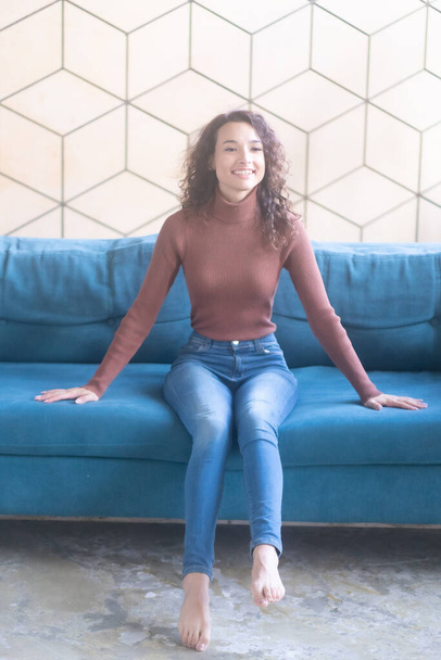 młoda piękna kobieta siedzi na kanapie w dżinsach - Zdjęcie, obraz