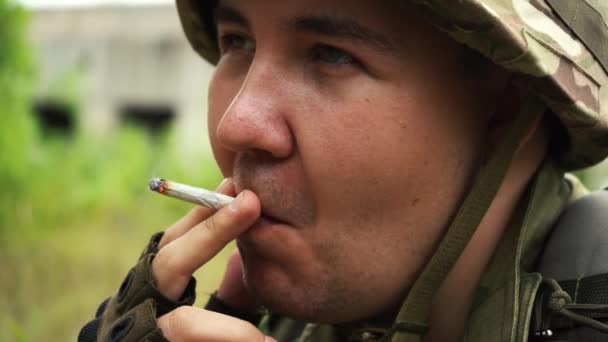 Человек в камуфляжной форме курит сигарету на остановке - Кадры, видео