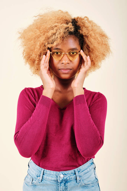 Nő afro frizurával napszemüveget visel, miközben komolyan néz a kamerába. - Fotó, kép