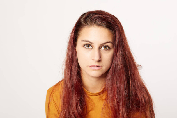 beautiful girl of 20 looking intensely at the camera with a neutral expression. Nice red hairstyle and orange sweater - Фото, изображение