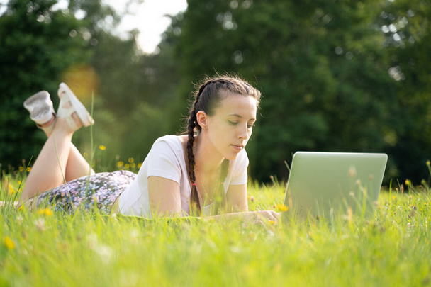 外で仕事だ。学生の女の子は、夏の公園でラップトップ、コンピュータタブレットで動作します。女性の屋外とオンライン技術。オフィス距離教育の概念から逃れる - 写真・画像