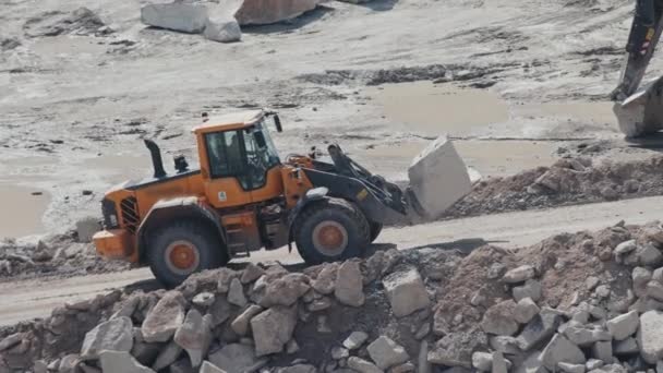 Tracking shot of irrecognizable worker driving loader along haul road in quarry and transporting block of granite - Metraje, vídeo