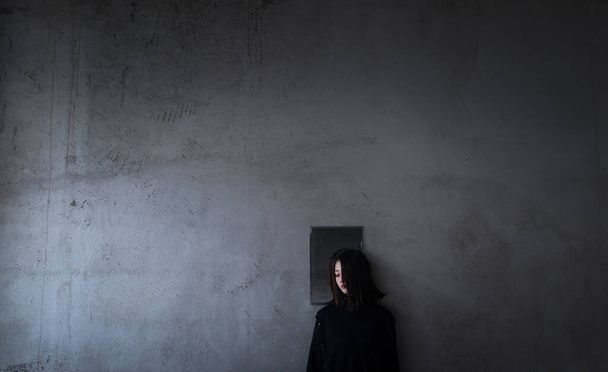 young woman with black hair in a dark room with a broken door - 写真・画像