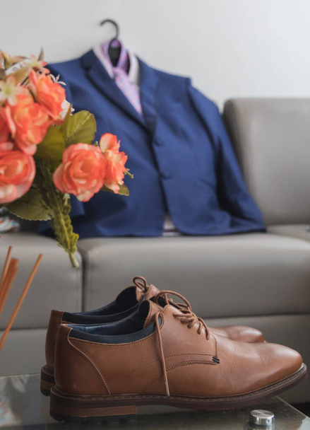 A vertical shot of a pair of brown derby shoes on the table with a suit in the background - Fotoğraf, Görsel