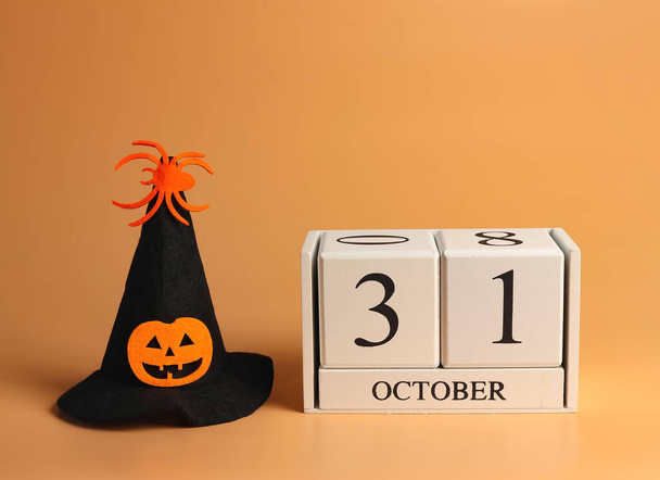 Front view of wooden calendar 31 October and Halloween witch hat decorated with pumpkin head and spider on orange background. Halloween costume concept. - Photo, Image