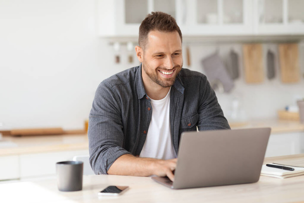 Przytulna praca w domu Młody szczęśliwy człowiek niezależny wykonawca pracujący na laptopie i uśmiechnięty, cieszący się zdalną pracą - Zdjęcie, obraz