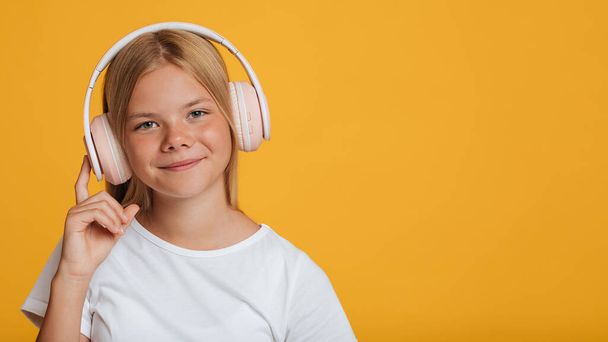 Smiling european teen girl in white t-shirt and wireless headphones listening music or lesson online - Foto, afbeelding