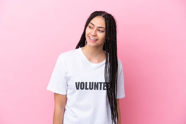 Teenager volunteer girl with braids isolated on pink background looking to the side and smiling - Foto, afbeelding