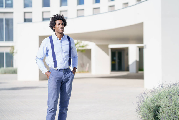 Black businessman wearing shirt and suspenders standing near an office building. - Фото, зображення