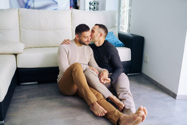 gej para siedzi w pobliżu w kanapie w domu w a romantyczny moment - Zdjęcie, obraz