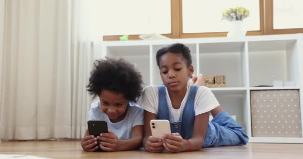 African siblings lying on floor having fun using smartphones - Πλάνα, βίντεο