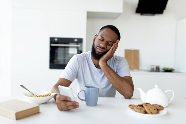 Hombre negro mensajes de texto en su teléfono inteligente desayunando en casa - Foto, Imagen