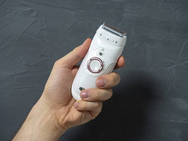 Electric epilator in white color in a man's hand on a gray textured background. Means for hair removal, beauty care, beauty - Fotoğraf, Görsel