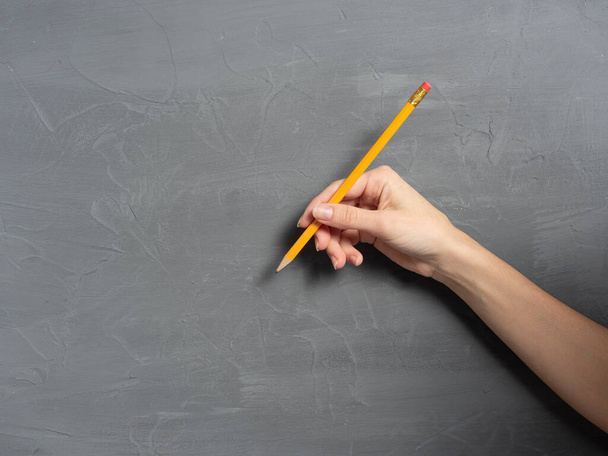 Die Hand einer Frau hält einen Bleistift auf einem grauen, strukturierten Hintergrund. Horizontales Foto, Kopierraum. - Foto, Bild