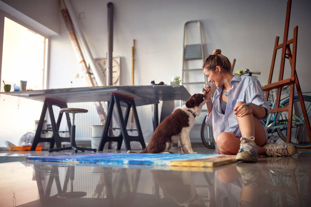 Young hot female artist playing with her dog in the studio - Фото, изображение