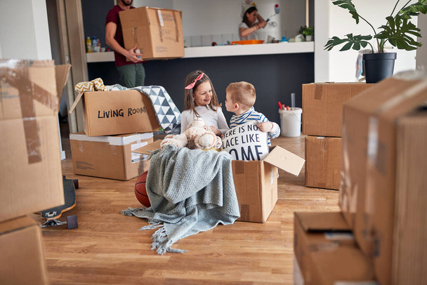 minor caucasian brother and sister, playing in empty cardboard box, happy in new apartment, with their parents in the background. new apartment, new begining - Φωτογραφία, εικόνα