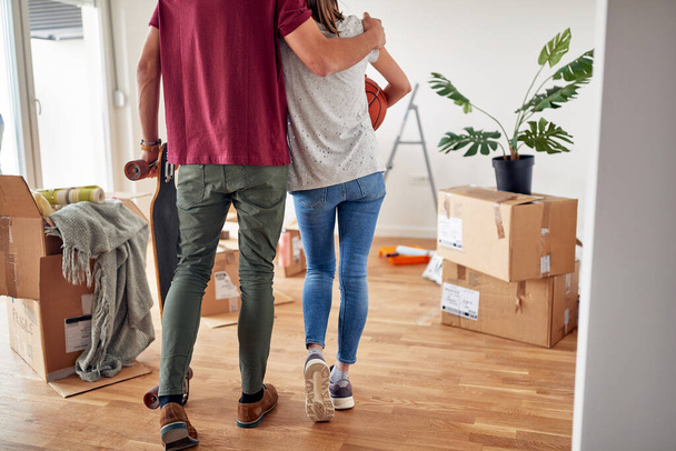 detail, cropped image of young male hugging his female partner in new apartment, holding skateboard, while she caring basketball - Фото, изображение