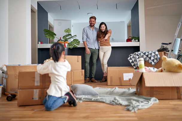 happy family -mother father and girl move to new apartment and unpack boxes - Photo, image