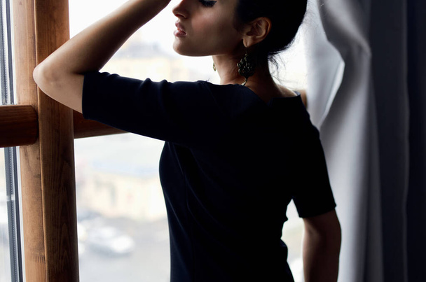 beautiful woman in a black dress near the window posing elegant style - Foto, Imagen