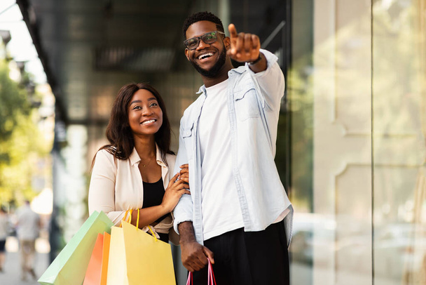 Excited black couple with shopping bags pointing aside - Foto, Imagen