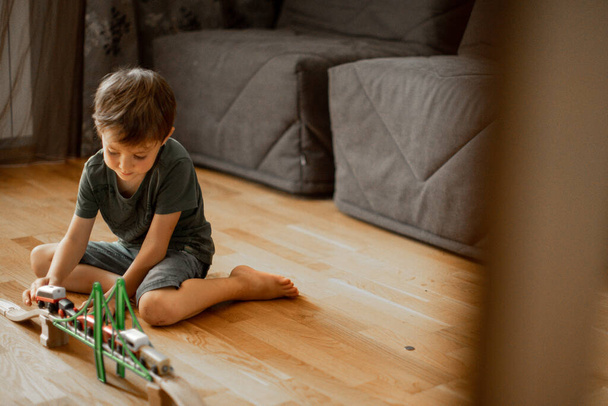 un niño de cinco años en casa en el suelo jugando con un ferrocarril de madera - Foto, Imagen