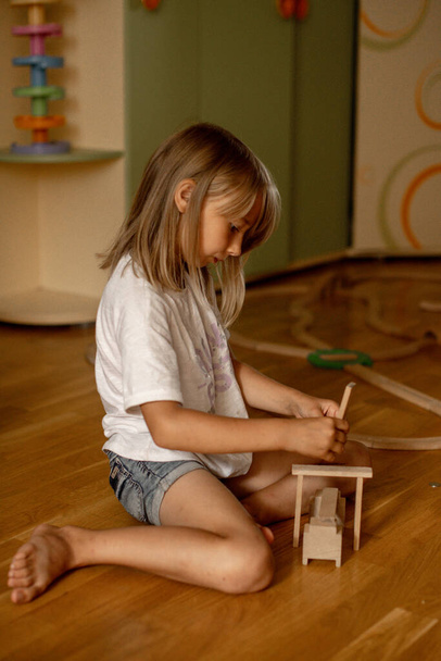 girl 7 years old plays at home with toys. Girl builds a tower from wooden  - Foto, Imagen