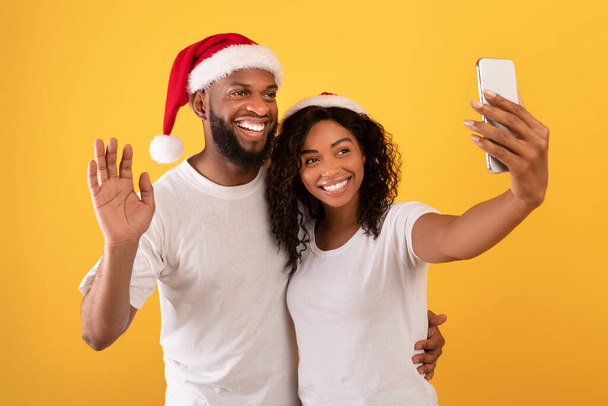 Ευτυχισμένο αφρικανικό ζευγάρι αμερικανική βίντεο καλώντας την οικογένεια κατά τη διάρκεια της Πρωτοχρονιάς και των Χριστουγέννων διακοπές, κίτρινο φόντο - Φωτογραφία, εικόνα