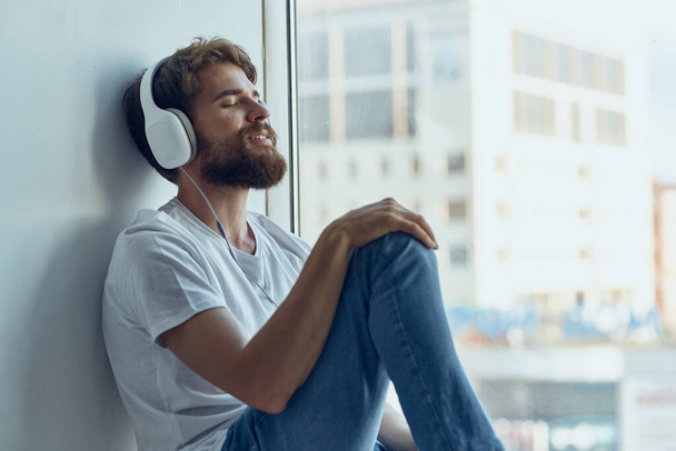 man in white t-shirt sitting on the windowsill in headphones in headphones - Foto, immagini