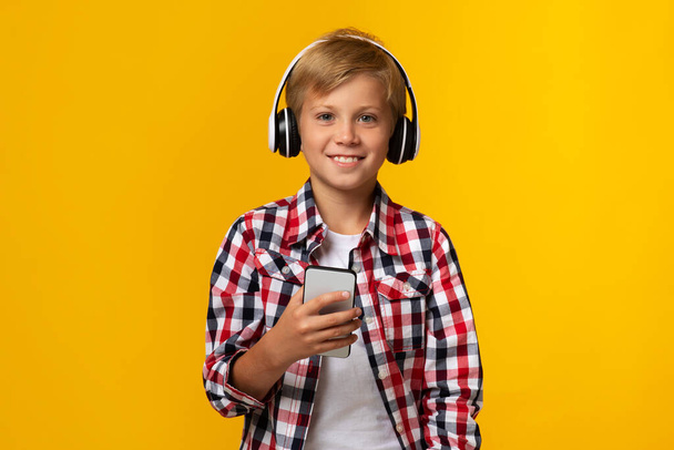 スマートフォンを持っているヘッドフォンで幸せな白人の少年,チャット - 写真・画像