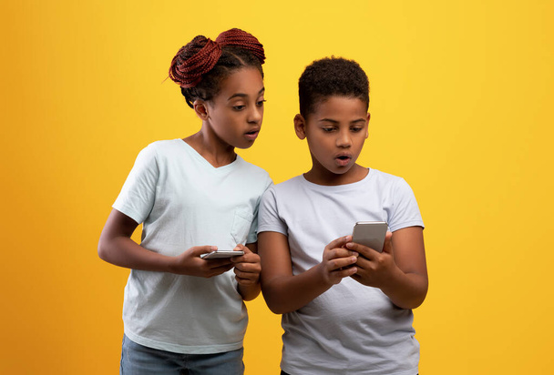 Shocked hermano negro y hermana usando teléfonos inteligentes - Foto, Imagen