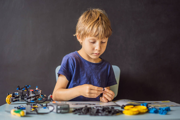 Vrolijke slimme school jongen aan tafel zitten en thuis een robot apparaat bouwen - Foto, afbeelding