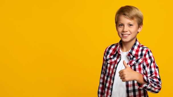 Χαρούμενη αυτοπεποίθηση Ευρωπαϊκό έφηβος αγόρι δείχνει τον αντίχειρα μέχρι κοιτάζοντας κάμερα, σε κίτρινο φόντο - Φωτογραφία, εικόνα