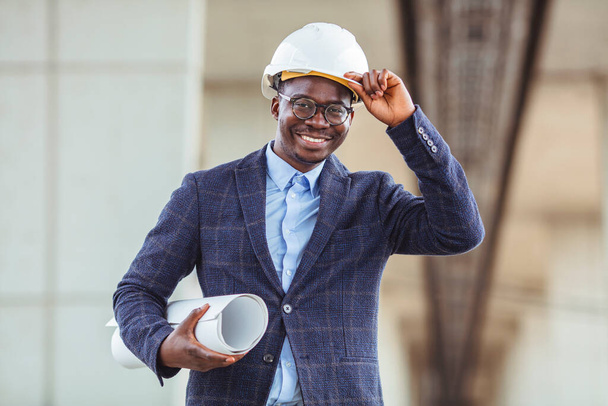Portrait of multiethnic architect with blueprints. Mature African American contractor holding roll of architectural projects while looking at camera. Happy man in casual standing outdoor  - Fotoğraf, Görsel