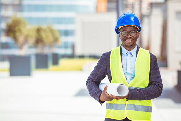 Successful male architect at building site looking at camera. Confident construction manager wearing blue helmet and yellow safety vest with copy space. Portrait of successful mature civil engineer. - Fotó, kép
