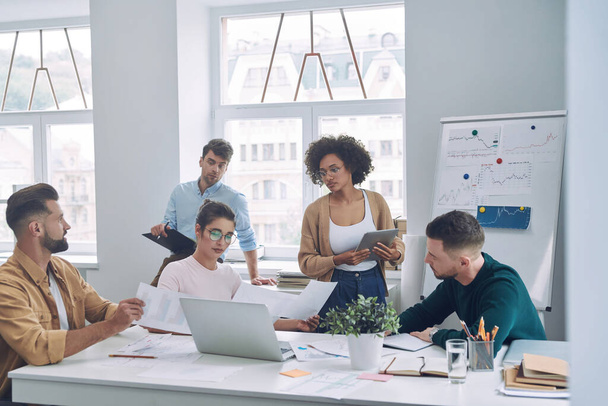 Група впевнених молодих людей у розумному повсякденному одязі обговорює бізнес під час зустрічі в офісі
 - Фото, зображення