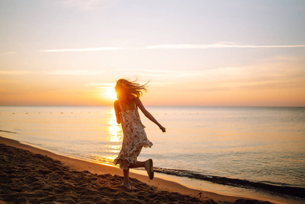 Young woman walks along seashore at sunset. Travel, weekend, relax and lifestyle concept. - Фото, зображення
