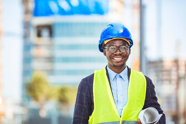 Close-up portrait of professional architect in hard hat looking at camera. Confident architect standing at construction site. Portrait of African American Engineer at a construction worksite. Looking at camera. - Foto, imagen
