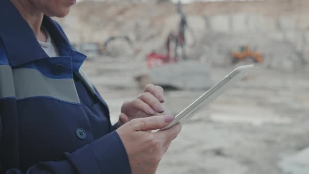 Tracking close up shot of middle-aged female supervisor in uniform, safety goggles and hard hat typing on tablet and doing inspection in granite quarry - Footage, Video