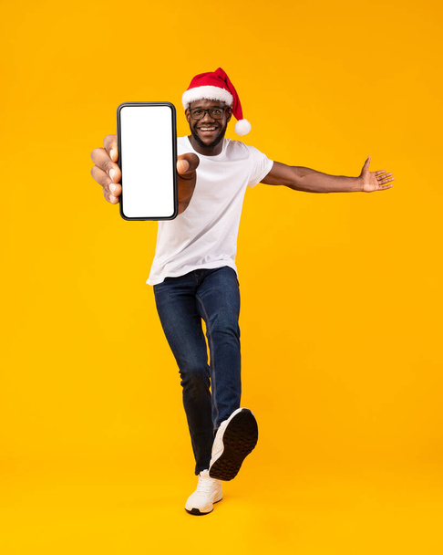 Hombre negro que muestra la pantalla del teléfono inteligente para la publicidad de Navidad en el estudio - Foto, imagen