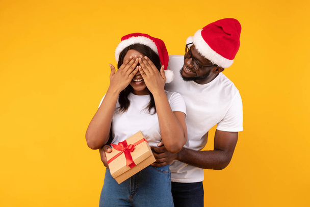 Afro-Amerikaanse man Verrassende vriendin met kerstcadeau, gele achtergrond - Foto, afbeelding