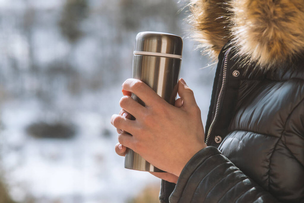 Una chica en una chaqueta de invierno con un termo de café o té en la mano en el balcón en invierno
 - Foto, imagen
