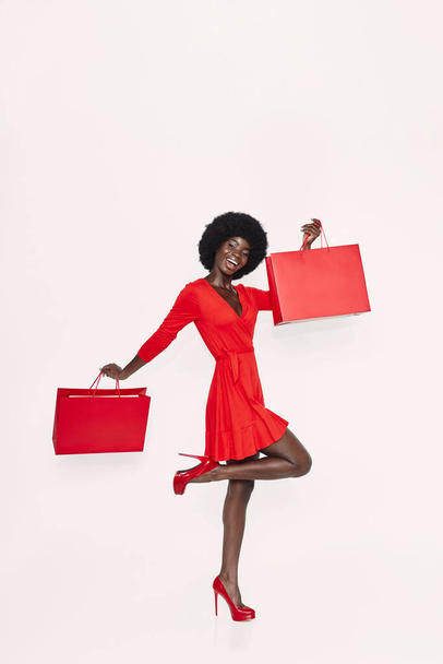 Full length of beautiful young African woman in red dress carrying red shopping bags - Photo, image