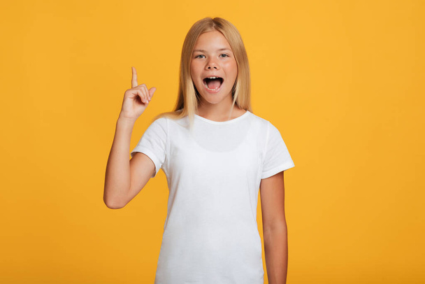 Surprised cheerful caucasian teen girl in white t-shirt with open mouth showing thumb up - Фото, изображение