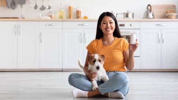 Vrolijke aziatische dame met schattig hondje tonen huisdieren supplement pot - Foto, afbeelding