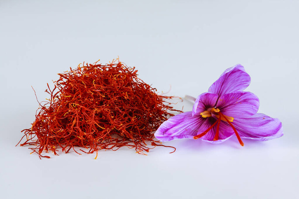 A bunch of saffron stigmas together with a crocus flower lie on a white background. The most expensive spice in the world. Saffron has a persistent aroma. - Photo, Image